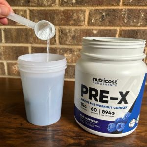 hand pouring scoop of nutricost pre-x xtreme pre workout into shaker bottle