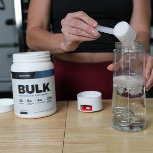 athlete pours a scoop of transparent labs bulk pre workout into a bottle with water in it