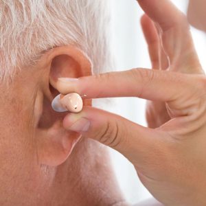 a hand is putting the hearing aids audien atom pro 2 into old man's ear