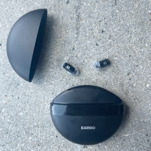 a pair of eargo 7 rechargeable hearing aids next to their charging case