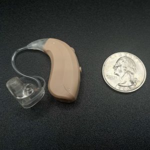 Close-up image of a MDHearing Volt hearing aid next to a quarter coin for size comparison