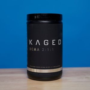 a closeup of a canister of Kaged BCAA 2:1:1 powder on a wood surface against a blue background