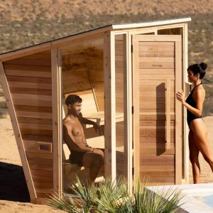 a Plunge outdoor sauna next to a pool or fountain in the desert, with a man lounging inside and a woman entering