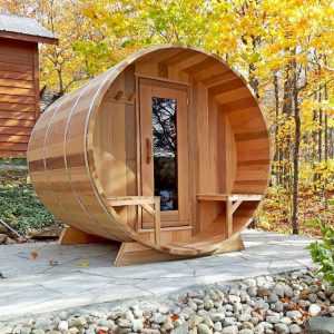a sun home canadian cedar barrel sauna set up outside on a stone patio, with yellow-leaved trees in the background