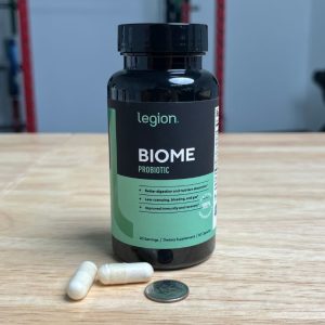 bottle of legion biome probiotic with capsules next to dime for size comparison