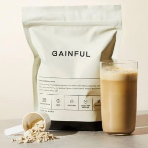 a bag of gainful protein shake next to scooper and mixed shake in a glass