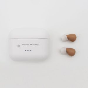 a pair of audien atom2 pro rechargeable hearing aids next to charging case