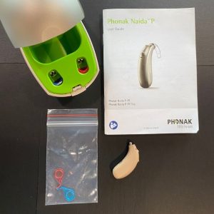 the phonak naida P on a table next to the manual, charging case, and accessories