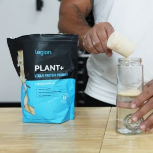 a person dumping a scooping of legion plant plus vegan protein powder into a shaker bottle