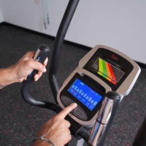 A hand presses a button on a Sunny Health & Fitness Smart Recumbent elliptical.