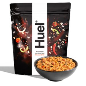 Huel Mexican Chili, a nutritionally complete food in an instant meal delivery format, featuring a rich blend of spicy ingredients in a convenient, black resealable bag, alongside a bowl of prepared chili for a quick and healthy meal.