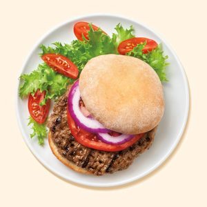 A healthy Nutrisystem meal featuring a grilled beef burger patty on a bun, garnished with fresh lettuce, tomato slices, and red onion rings, served with cherry tomatoes on a white plate.