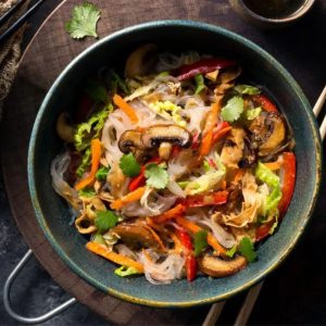 A meal from Sunbasket meal delivery service featuring a vibrant dish of stir-fried glass noodles with mushrooms, bell peppers, shredded cabbage, carrots, and fresh cilantro, served in a dark bowl for a nutritious and flavorful experience.