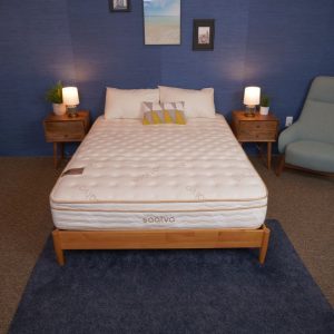 A bed with a white mattress and a quilted top surface, set in a bedroom with a navy blue wall and two wooden nightstands with lamps. The bed is neatly made with pillows.