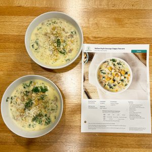 two bowls of Italian-style sausage zuppa toscana soup from a Home Chef meal delivery kit, next to the recipe card on a wooden counter
