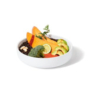 A white bowl with sliced sweet potatoes, broccoli, avocado, and a lime slice on a bed of black rice.