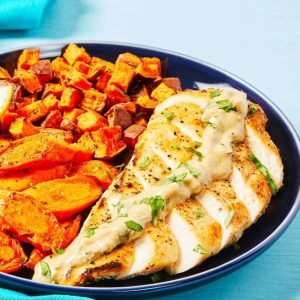 A plate with grilled chicken breast topped with sauce and served with roasted sweet potatoes.