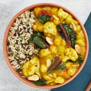 A bowl of rice and lentils with a vegetable curry including cauliflower, chard, chickpeas, and almonds.