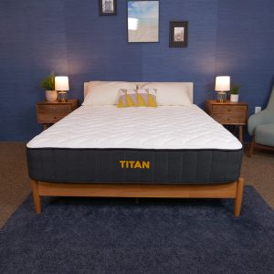 A Titan mattress on a wooden bed frame in a blue-themed bedroom, flanked by nightstands and lamps.