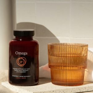 A stylishly designed bottle of LifeForce Omega dietary supplement, promoting cardiovascular health, insulin regulation, and metabolism, placed next to an orange-tinted glass.